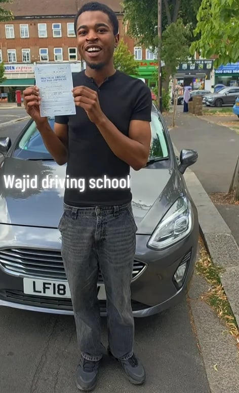 Young man smiling while holding a driving licence certificate next to a silver car
