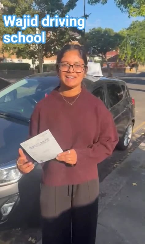 Young woman in glasses and a maroon sweater holding her certificate in front of parked cars
